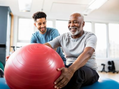 Physical therapist working with elder patient, physiotherapy, helping old retired african american pensioner man in a clinic, therapy